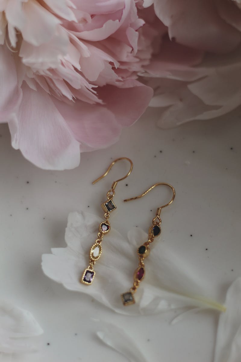 Luxurious gold earrings with gemstones on a soft pink floral backdrop.